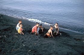 Kinder am Strand mit schwarzem Sand bei Galela