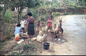 Frauen und Kinder an einer Wasserstelle füllen Kanister mit Trinkwasser