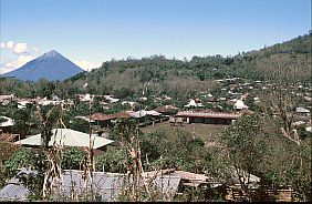 Traditionell angelegtes Dorf mit Wellblechdächern, im Hintergrund der Vulkan Ebulobo 