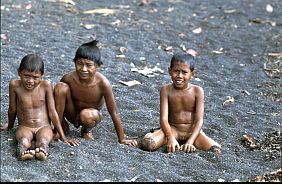 Drei nackte Jungen sitzen am schwarzen Strand von Labuhan Kenanga