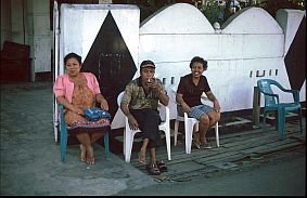 Mann und zwei Frauen sitzen vor ihrem Haus